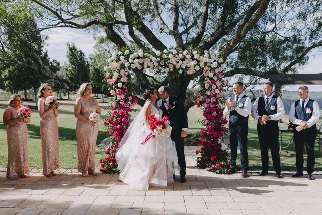 A bride and groom are kissing under a tree at their wedding ceremony.