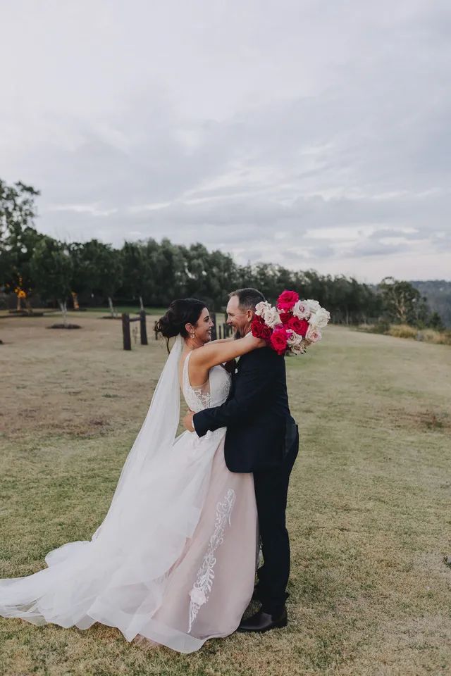A bride and groom are kissing in a field with a bouquet of flowers.