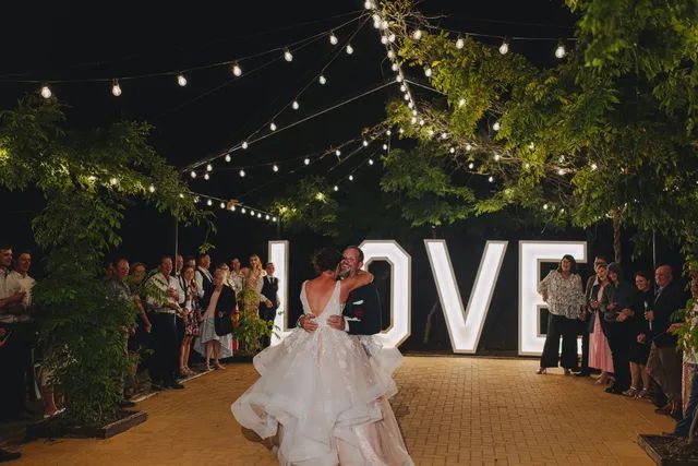 A bride and groom are dancing in front of a large love sign.