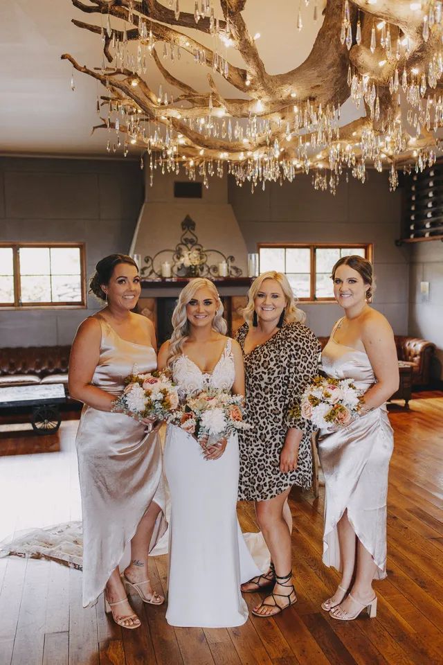 A bride and her bridesmaids are posing for a picture in a room with a chandelier.