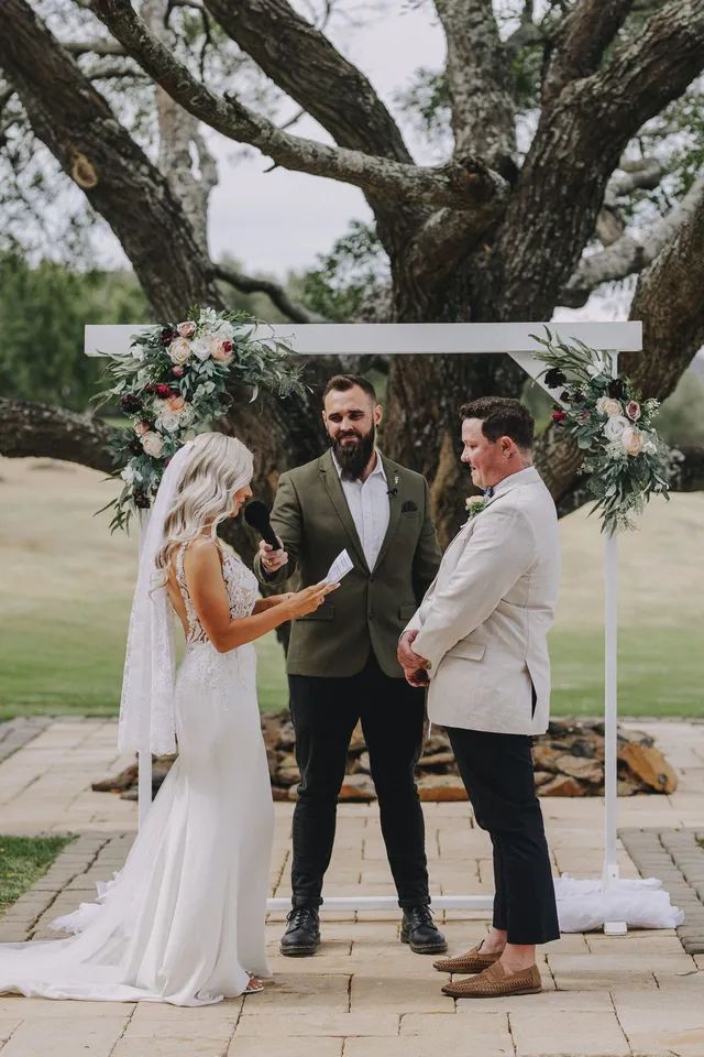 A bride and groom are standing under a tree during their wedding ceremony.