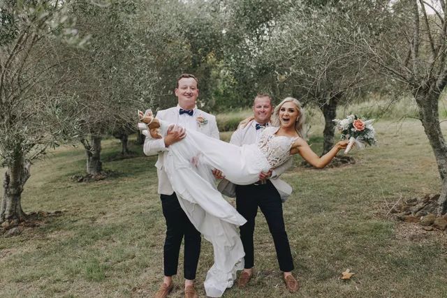 A man is carrying a bride in his arms in a field.