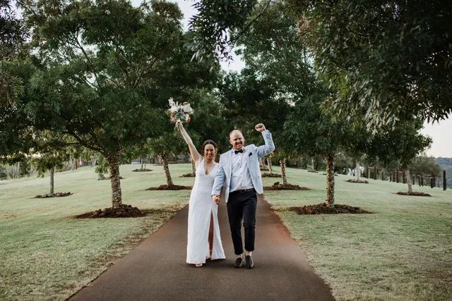 A bride and groom are walking down a path holding hands.