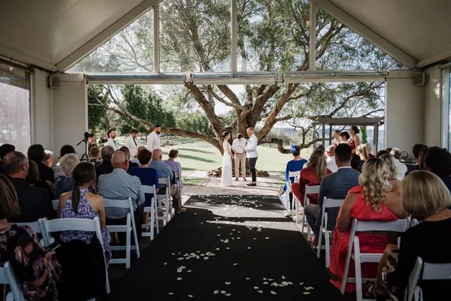 A group of people are sitting in chairs at a wedding ceremony under a tree.