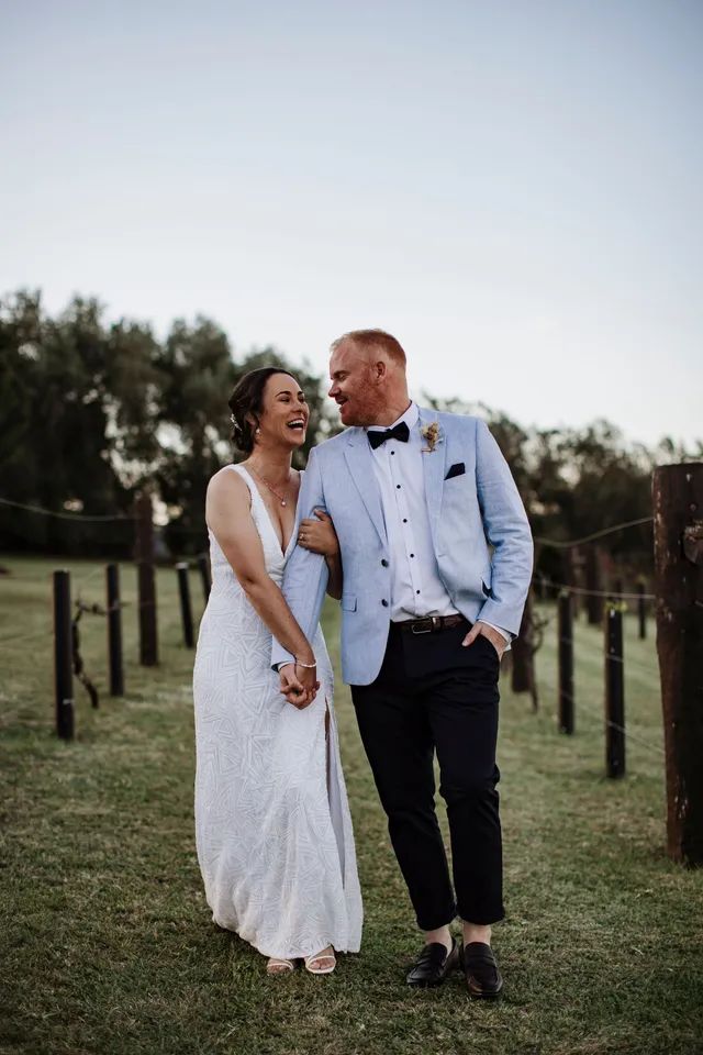 A bride and groom are standing next to each other in a field.