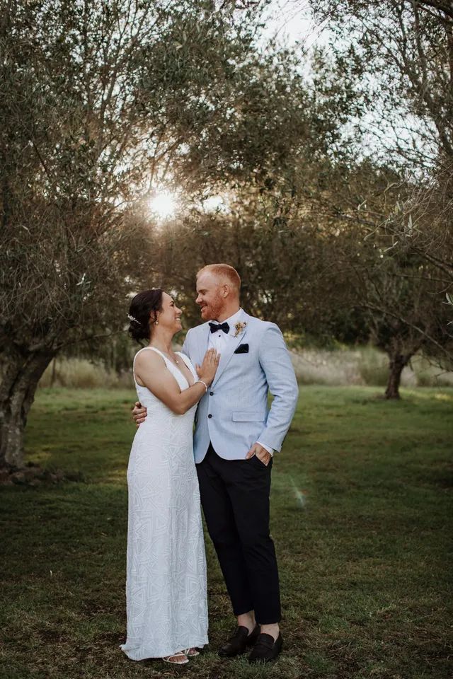 A bride and groom are standing next to each other in a field.
