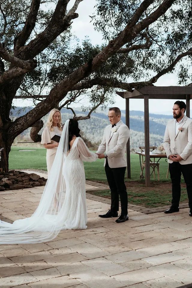 A bride and groom are holding hands during their wedding ceremony under a tree.