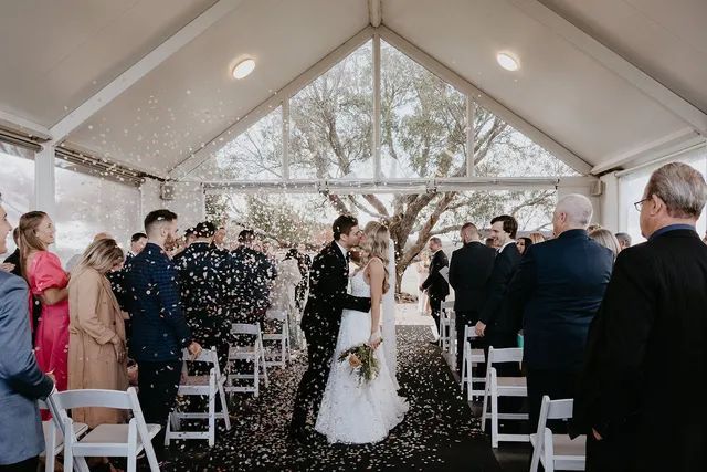 A bride and groom are kissing in front of a crowd of people at their wedding ceremony.