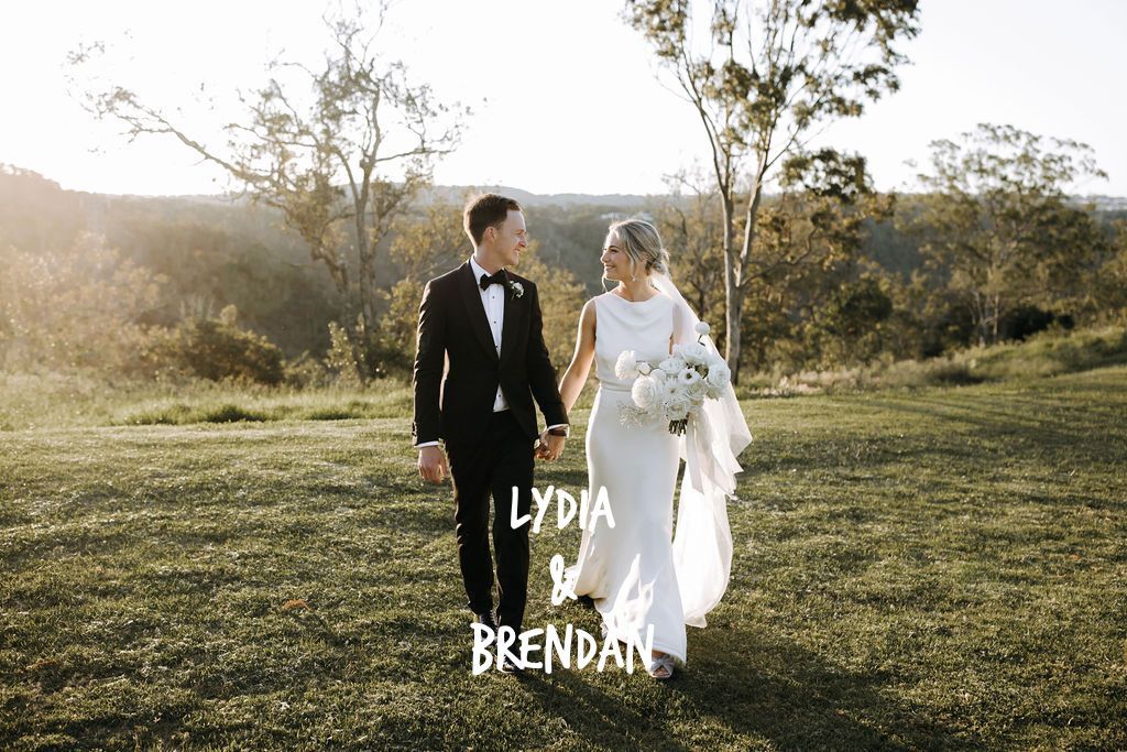 A bride and groom are walking in a field holding hands.