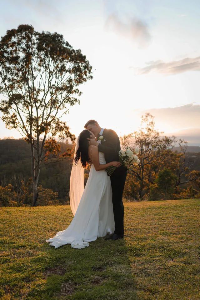 A bride and groom are kissing in a field at sunset.