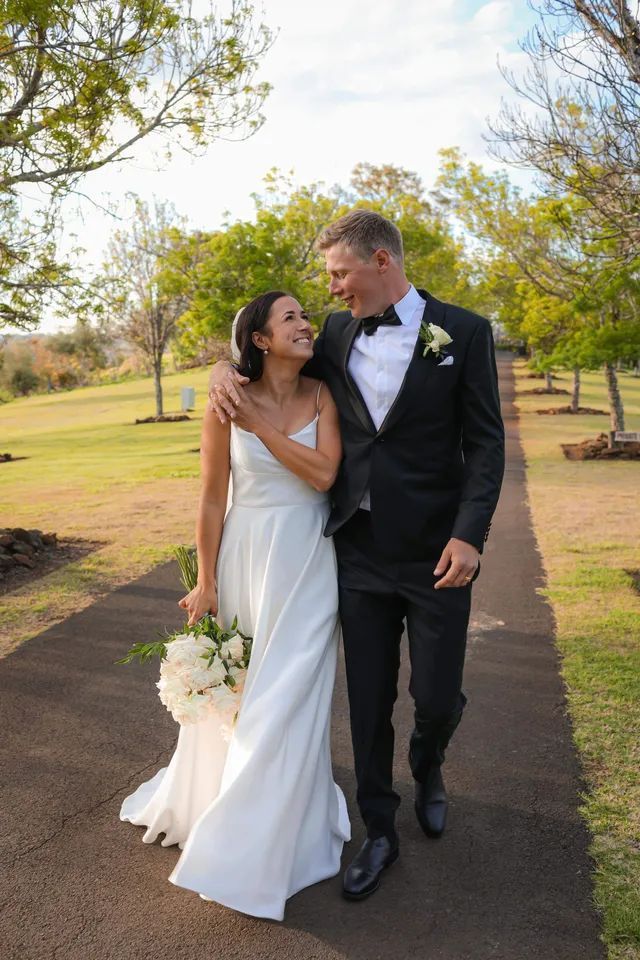 A bride and groom are walking down a path in a park.