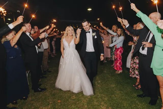 A bride and groom are walking through a tunnel of sparklers.