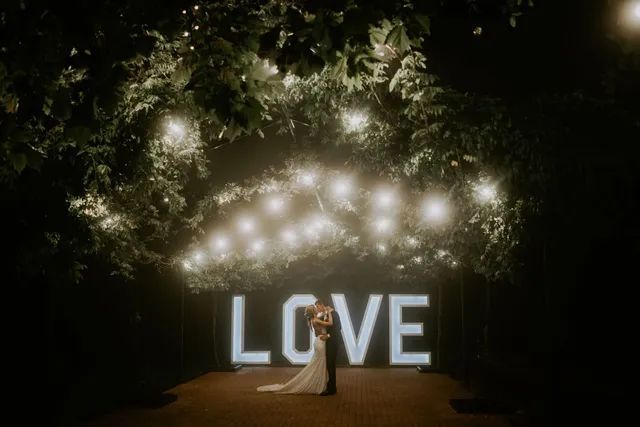 A bride and groom are standing in front of a large love sign.