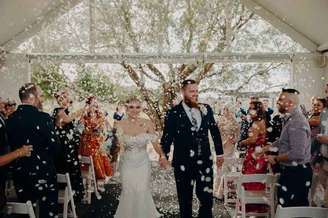 A bride and groom are walking down the aisle surrounded by confetti.