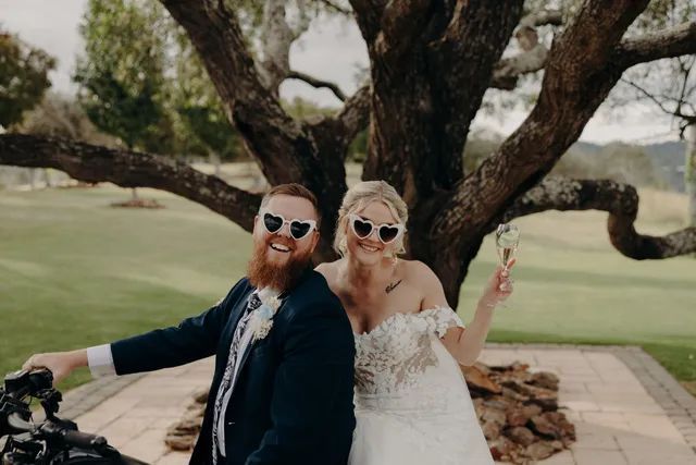A bride and groom are posing for a picture in front of a tree.