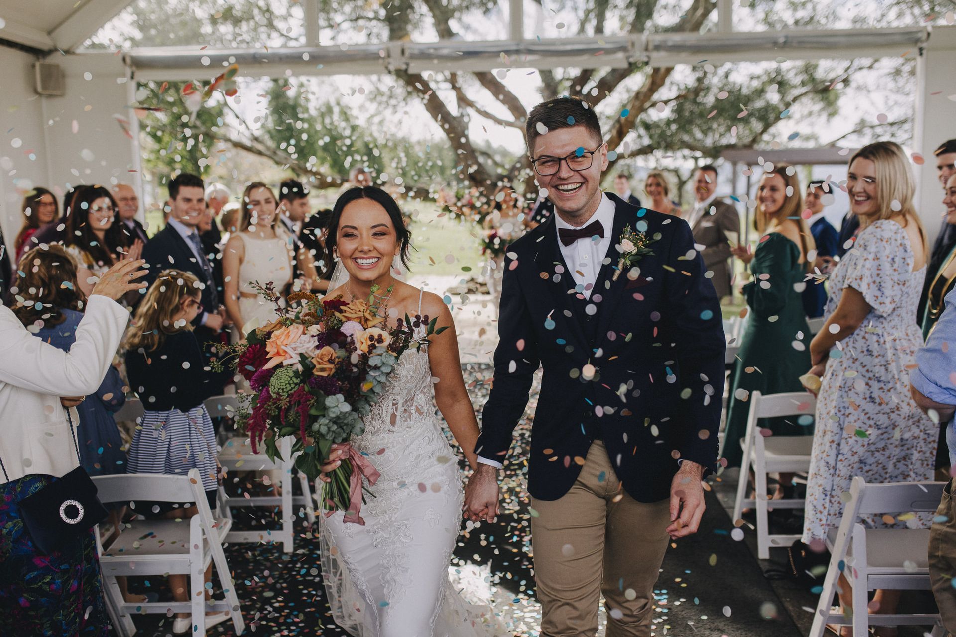 A bride and groom are walking down the aisle surrounded by confetti.