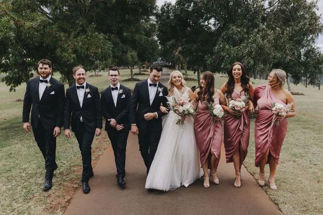 A bride and groom are walking down a path with their wedding party.