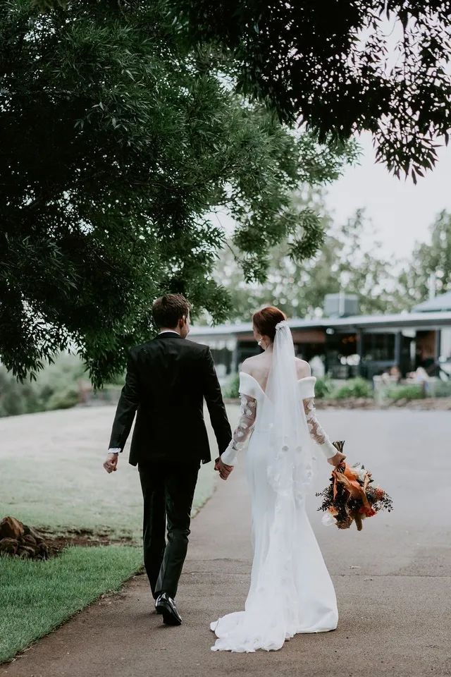 A bride and groom are walking down a sidewalk holding hands.