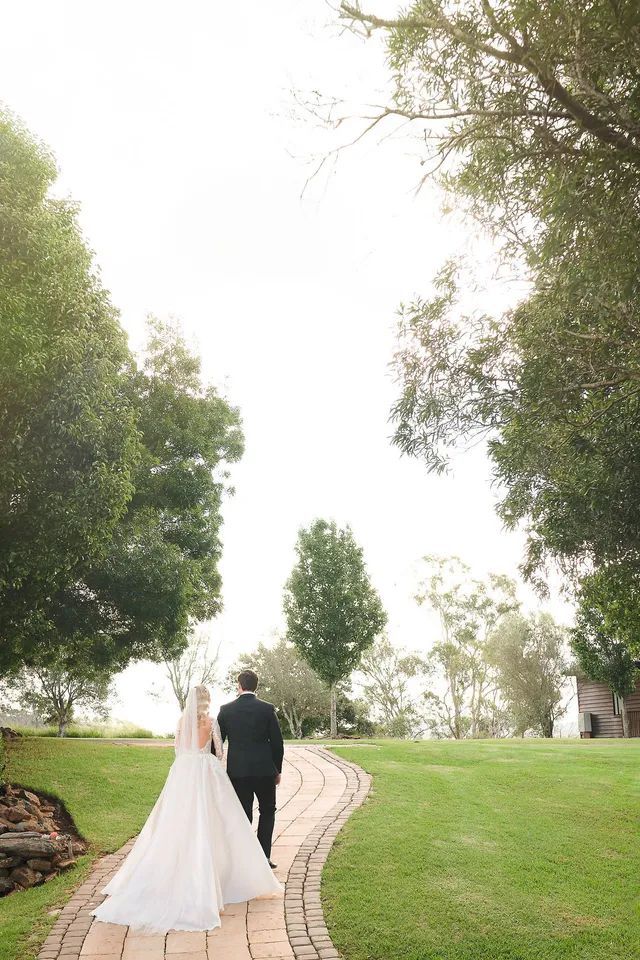 A bride and groom are walking down a path surrounded by trees.