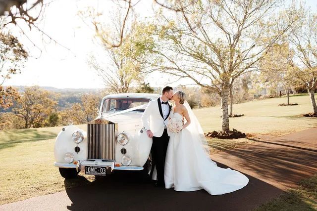 A bride and groom are kissing in front of a white car.