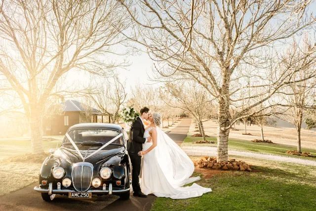 A bride and groom are posing for a picture in front of a wedding car.