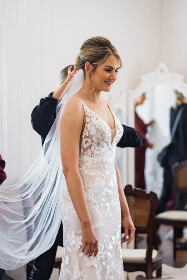 A woman in a wedding dress is getting her veil on.