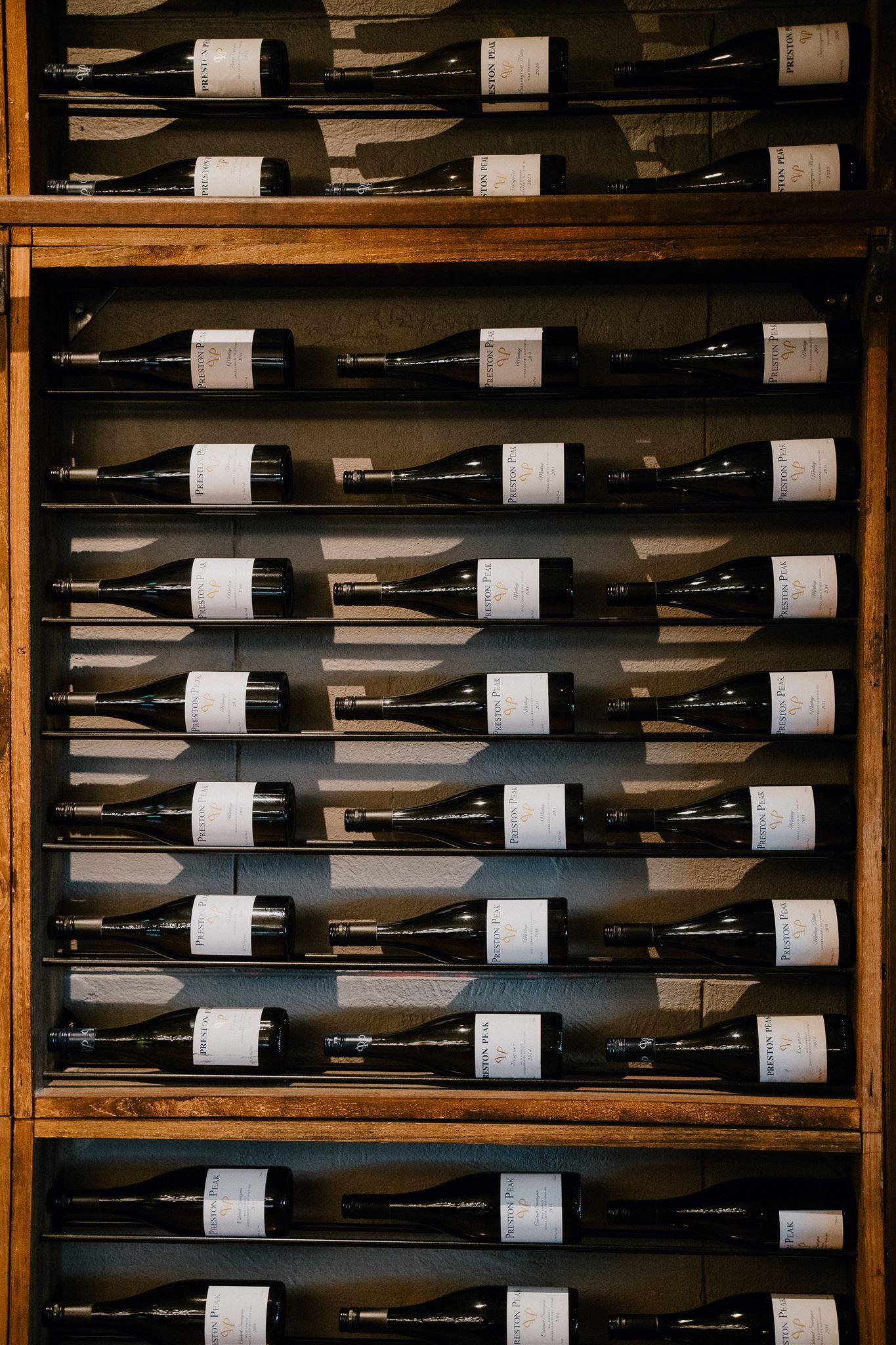 A row of wine bottles are lined up on wooden shelves.