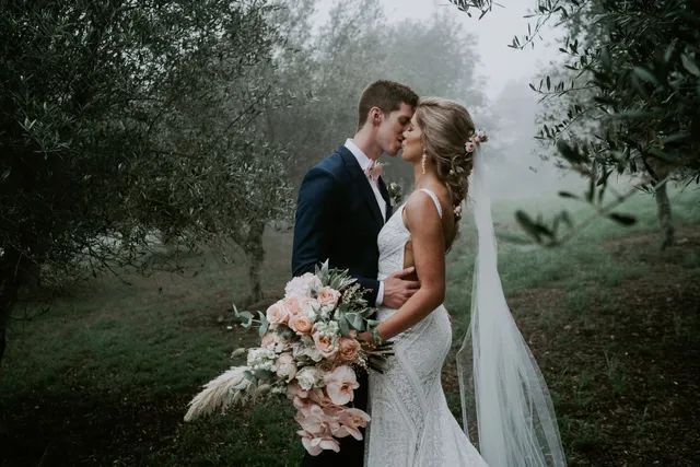 A bride and groom are kissing in the fog while holding a bouquet of flowers.