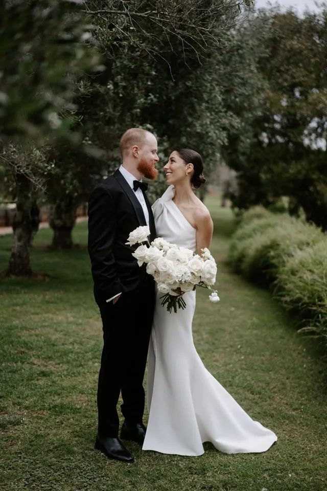 A bride and groom are standing next to each other in the grass.