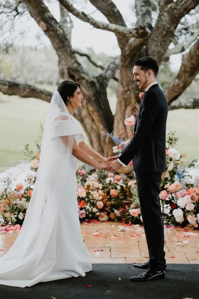 A bride and groom are holding hands during their wedding ceremony under a tree.