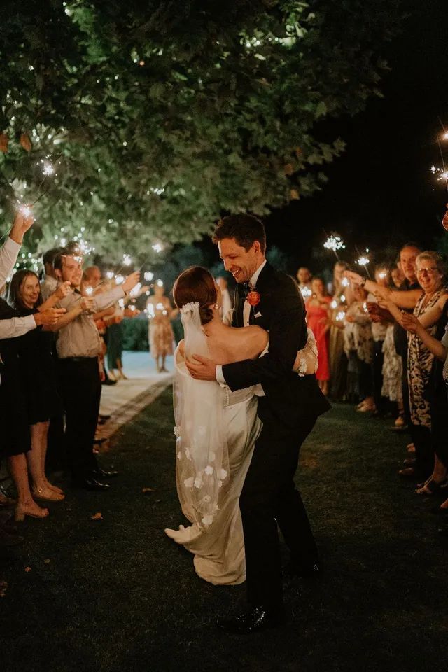A bride and groom are dancing in front of a crowd of people holding sparklers.
