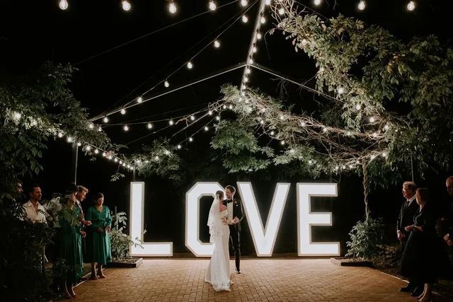 A bride and groom are dancing in front of a large love sign.