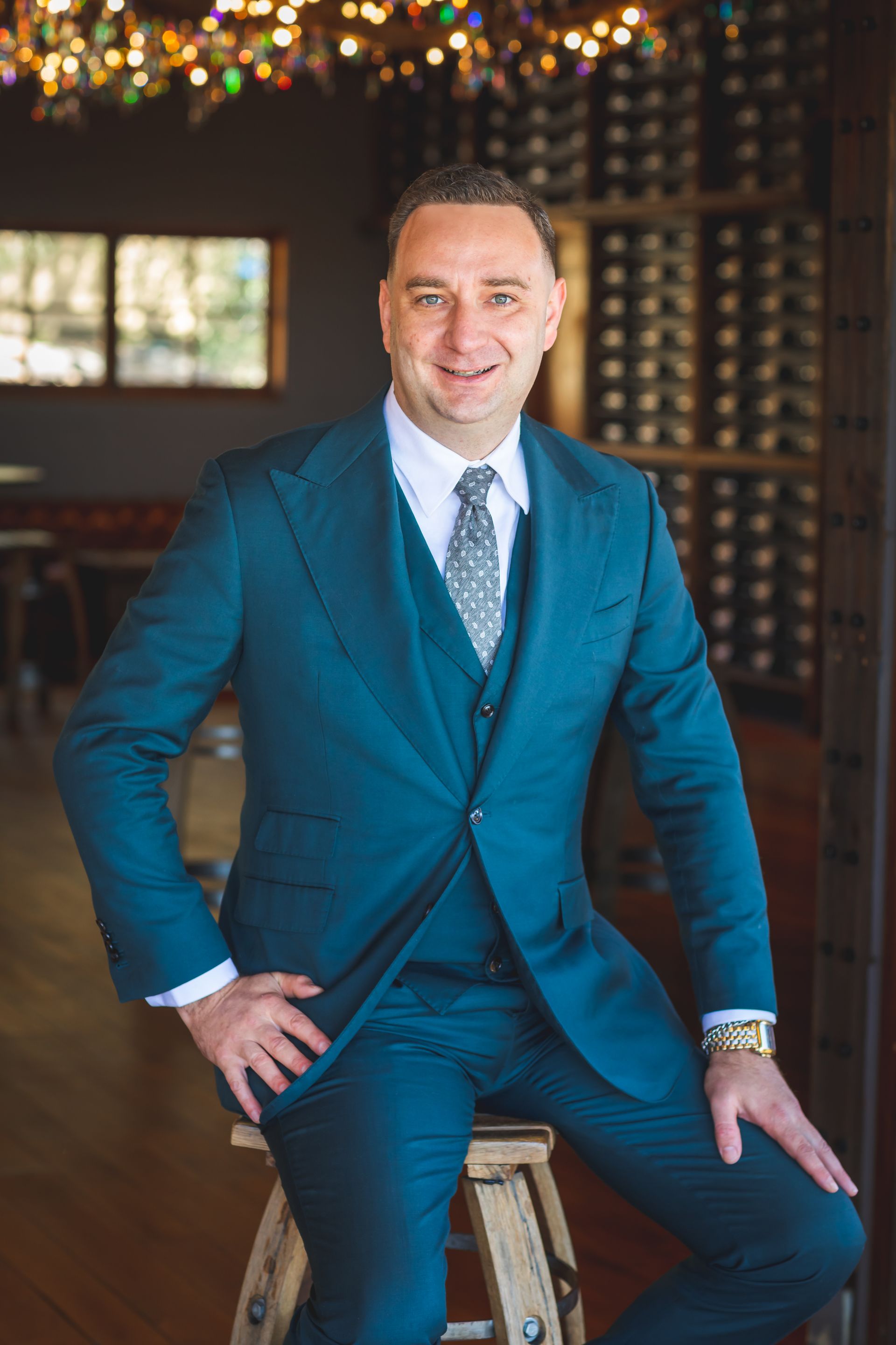 A man in a suit and tie is sitting on a stool.