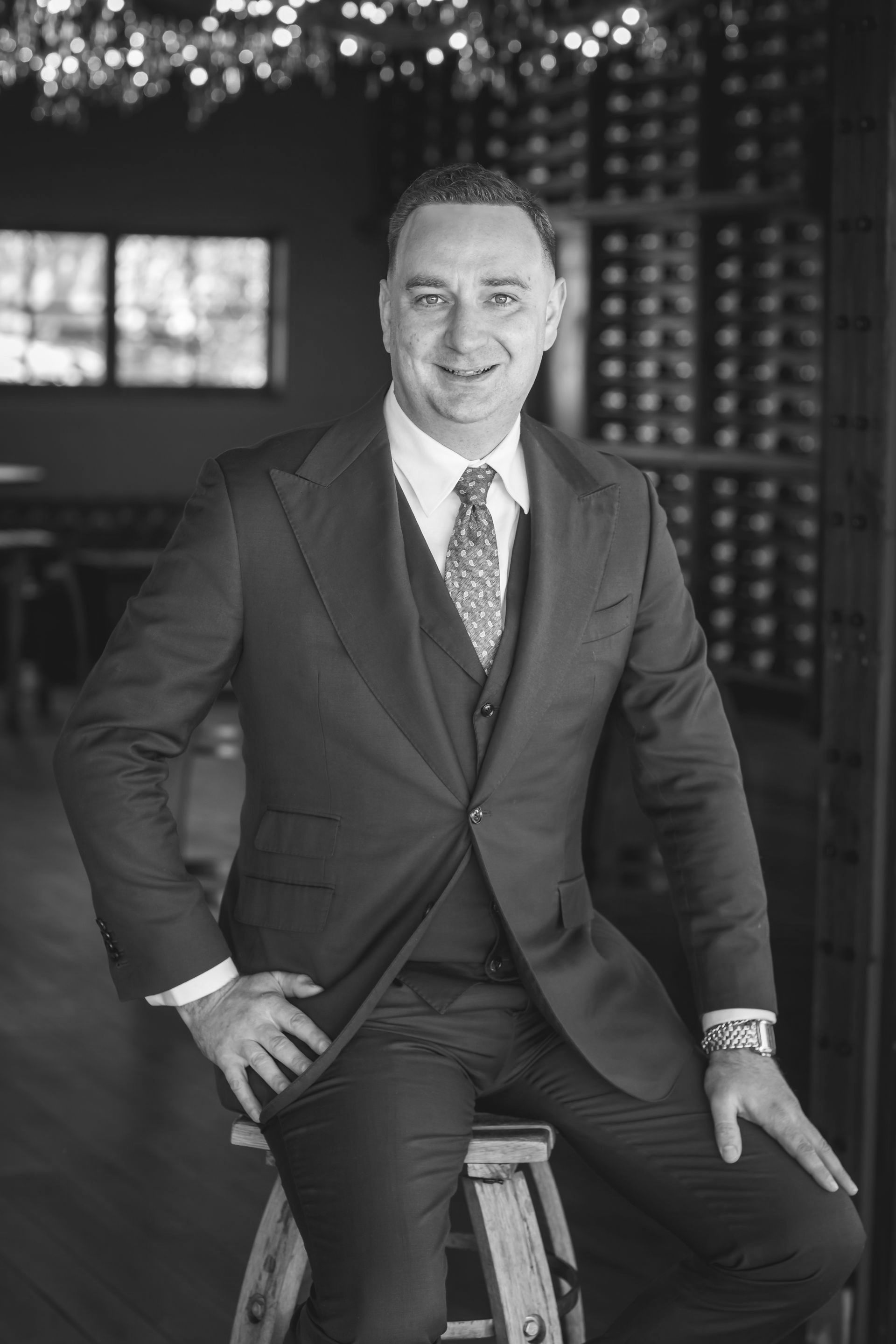 A man in a suit and tie is sitting on a stool.