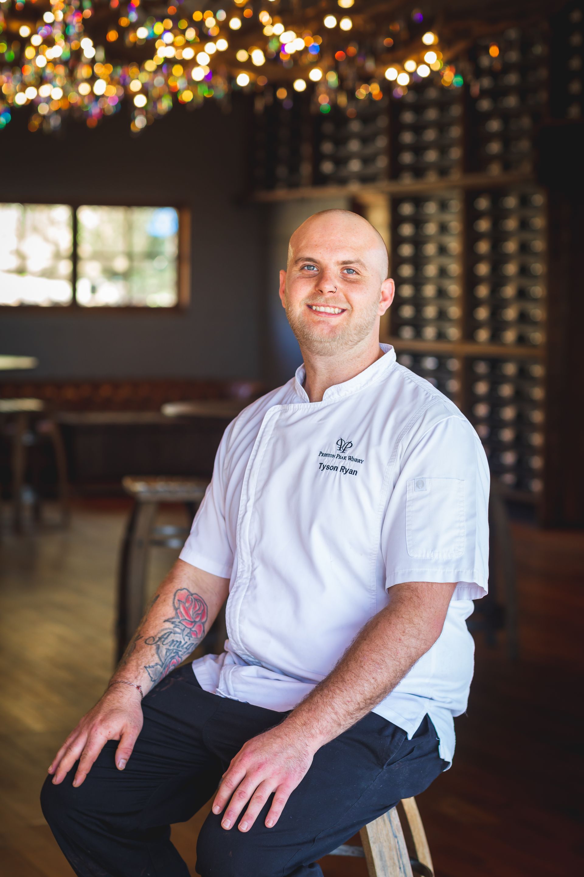 A man with a tattoo on his arm is sitting on a stool in a restaurant.