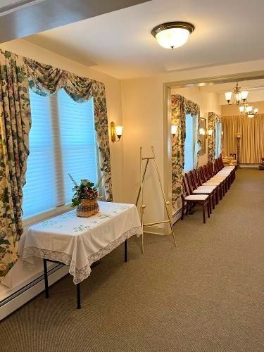 Interior room with windows, draped curtains, table with floral arrangement, chairs, and lighting.