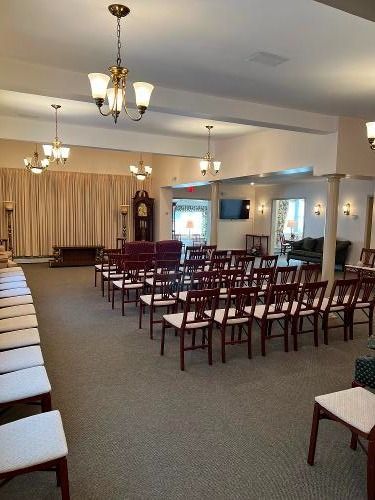Interior of a funeral home with rows of chairs facing a curtained area, chandelier lighting, and a clock.