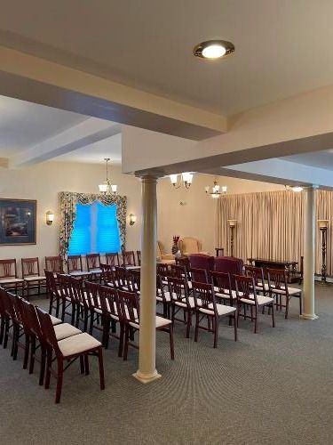 Funeral home interior with rows of chairs facing an area with a window and curtains.