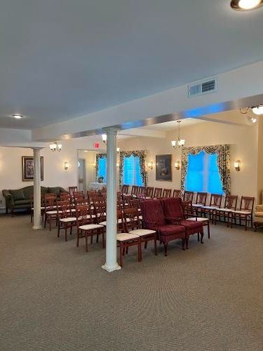 Interior of a funeral home with rows of chairs, windows with curtains, and pillars.