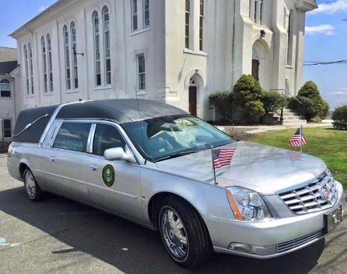 Silver hearse with American flag parked outside a white church.