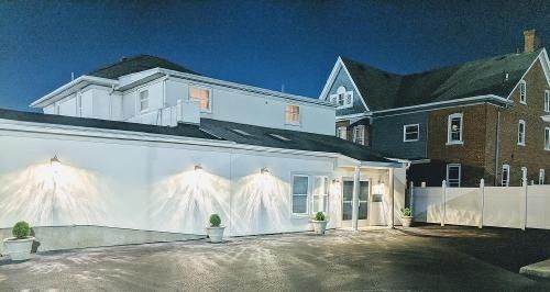 White building exterior illuminated by spotlights, night scene, with other buildings in the background.