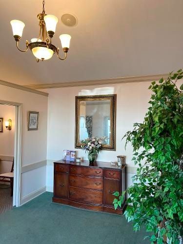 A formal room with a wooden cabinet, mirror, and chandelier. A potted tree is in the right corner.