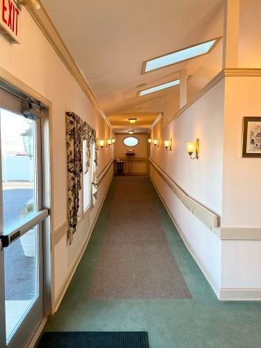 Long hallway with green carpet, beige walls, sconce lights, and an exit door.