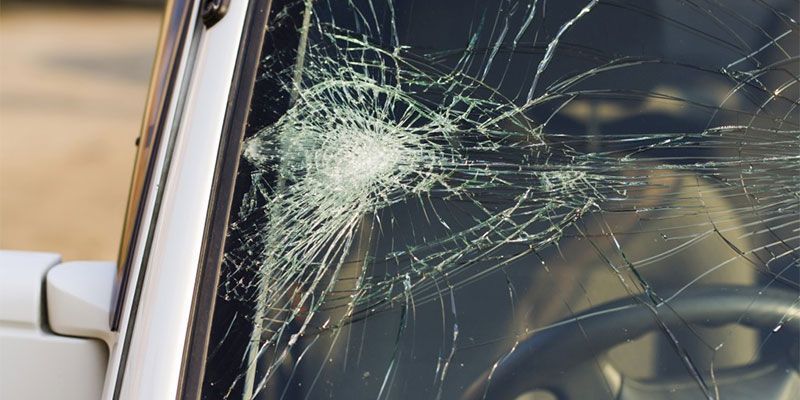 A man is driving a car with a broken windshield.