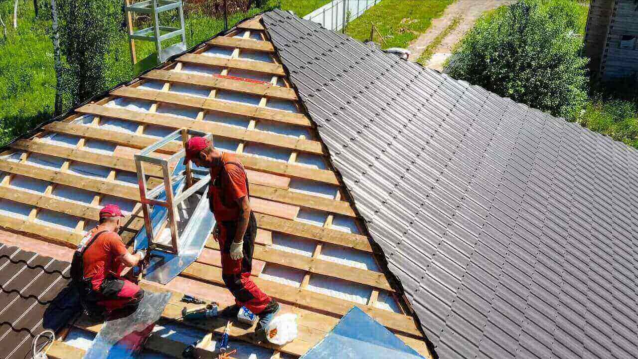 Two men installing metal roof on a house under construction.