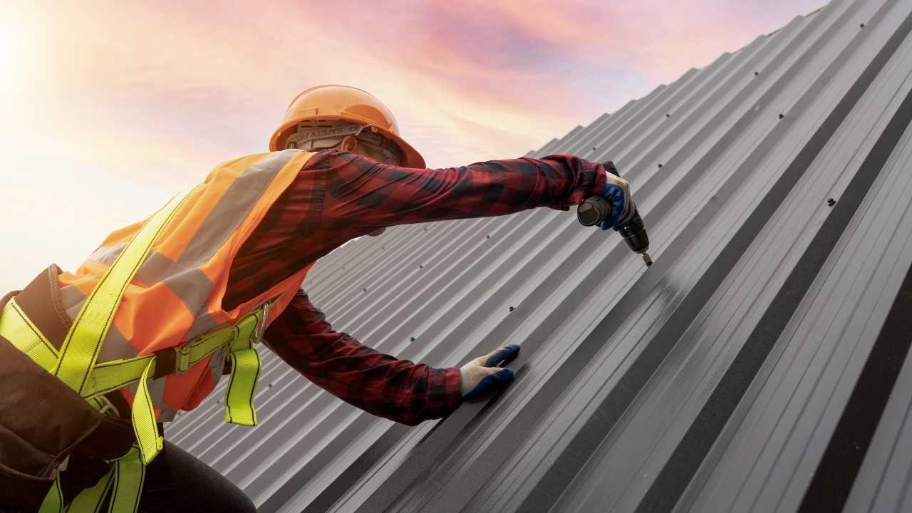 A man in safety gear diligently working on a metal roof.