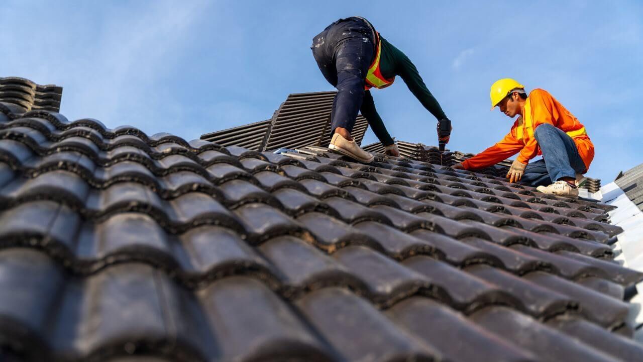 Two men working on a roof under a clear blue sky.