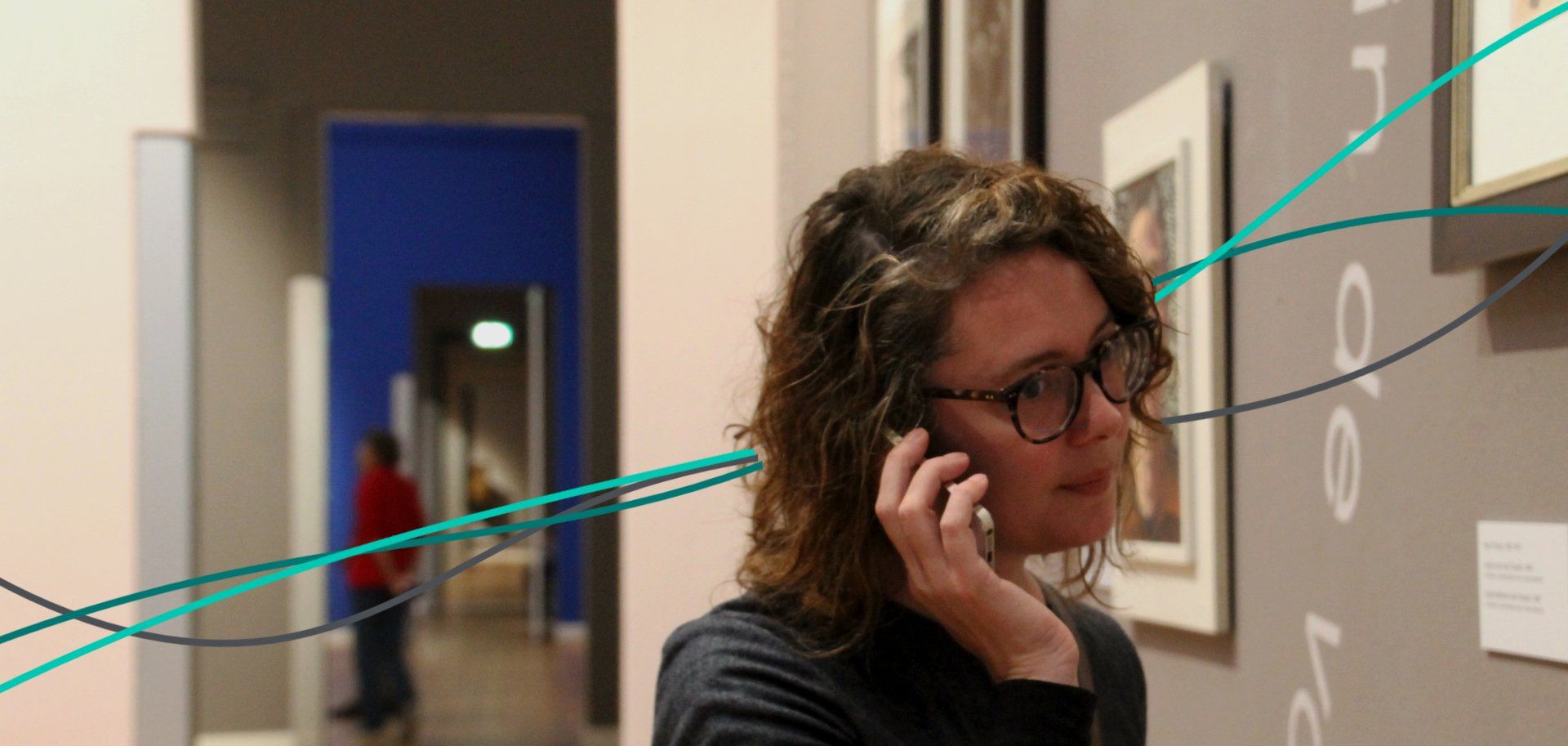 A woman listening to an audio guide in a museum with paintings on the wall and green lines flowing through the photo