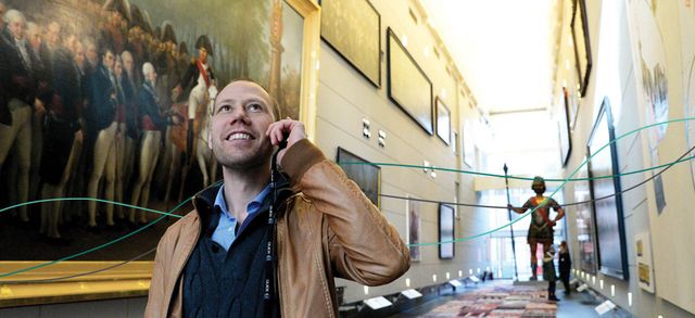 A man listening to an audio guide whilst walking through a gallery with green illustrated lines flowing through
