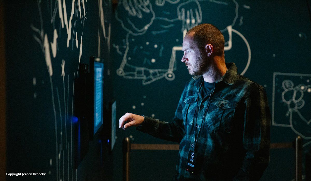 A man in a dark room looking at a brightly lit screen hanging on the wall